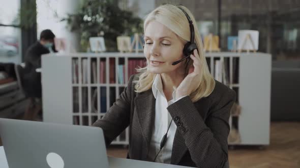 Middleaged Business Woman with Headset Working on Laptop in the Office and Advises Online