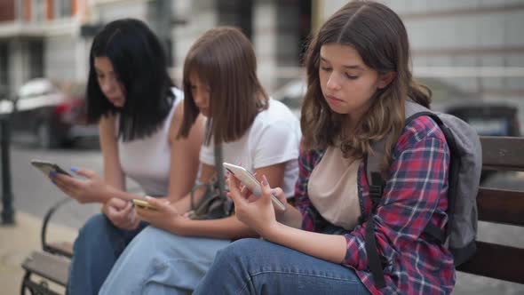 Bored Caucasian Teenage Girl Yawning Sitting on City Street with College Groupmates Surfing Social