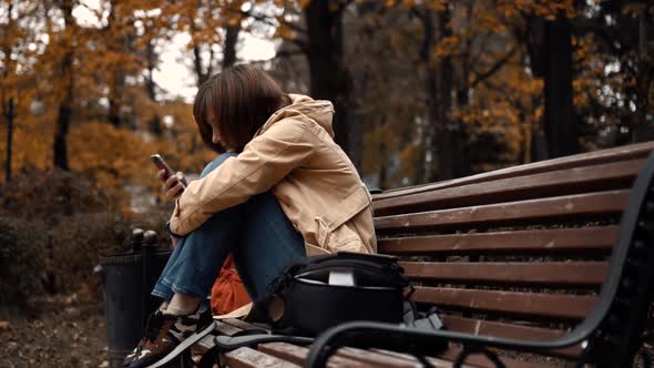 Young Girl Sitting Alone in a Park with a Phone