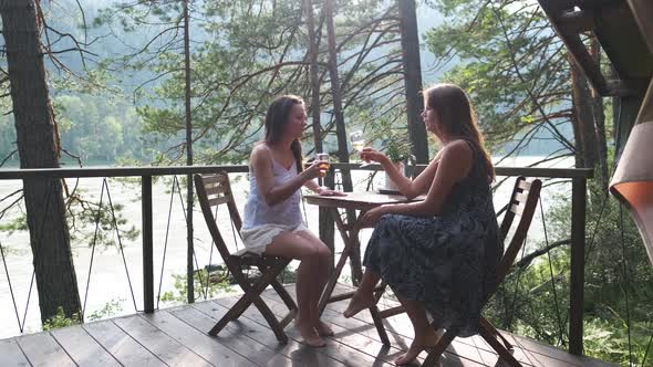 Two Attractive Girls Are Sitting at a Coffee Table on the Balcony, Enjoying Nature. Two Girlfriends