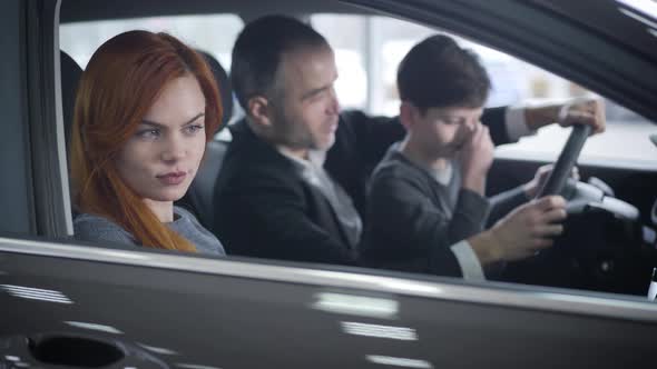 Side View of Beautiful Redhead Caucasian Woman Sitting in Car Salon with Family