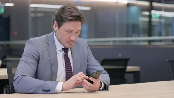 Middle Aged Businessman using Smartphone in Office 