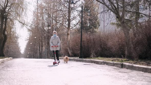 The Little Girl Is Driving a Scotter on a Park Alley