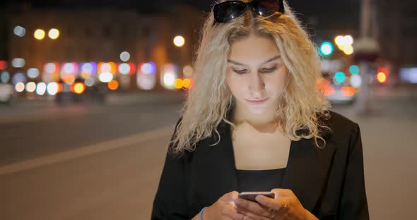 Lady Looks at Camera and Smiles Against Blurred Night Lights