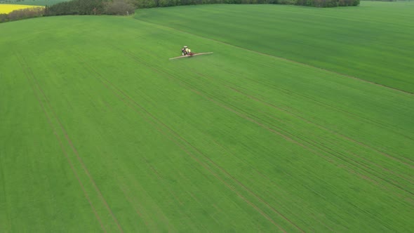 Aerial View of Farming Tractor Plowing and Spraying Green Wheat Field