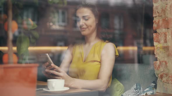 Attractive Young Lady Using Smartphone in Cafe Relaxing with Gadget and Coffee