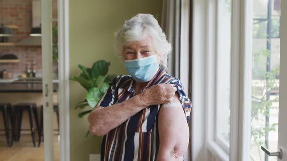Caucasian senior woman wearing face mask showing her vaccinated shoulder at home