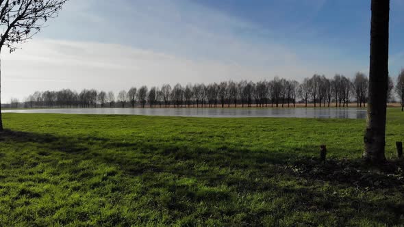 Flying Over Green Grass Towards Frozen River At Sandelingen Park In Hendrik-Ido-Ambacht, Netherlands