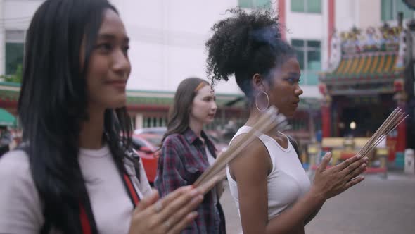 A group of multi-ethnic female friends praying at a Chinese shrine in Bangkok, Thailand.