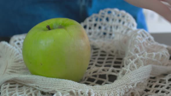 On the Dark Surface of the Countertop There is a White Fruit Net One Green Apple is Placed in It