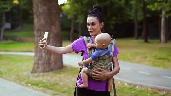 Young woman taking selfie while carrying baby in sling