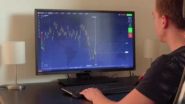 A Man Sits at a Table, Examines a Chart on a Computer Screen and Zooms Out