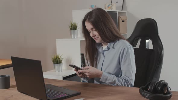 Girl Typing a Message on the Phone Using a Laptop