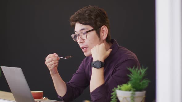 Asian man having a snack while looking at laptop while sitting at a cafe