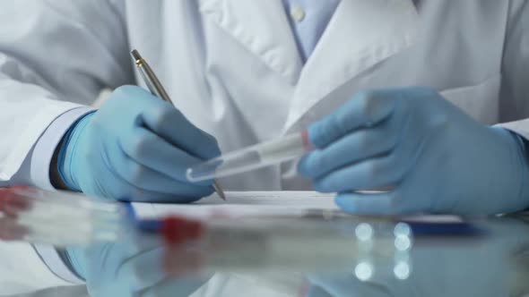 Lab Worker Filling in Test Results Forms, Holding Plastic Tube With HIV Sample