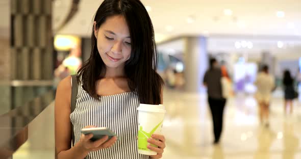 Woman using smart phone and holding coffee cup in shopping mall