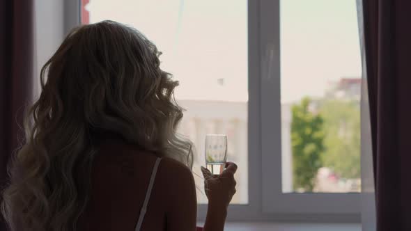 Woman with Long Curly Hair Holds Glass of Champagne in Room