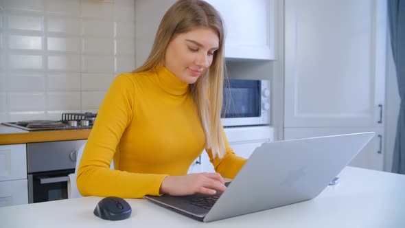 Young adult blond girl typing on laptop computer at home on lockdown in 4k video