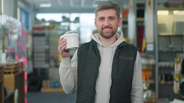 Handsome Cheerful Employee with Brown Eyes and Toothy Smile Posing with Tin of Paint in Hardware