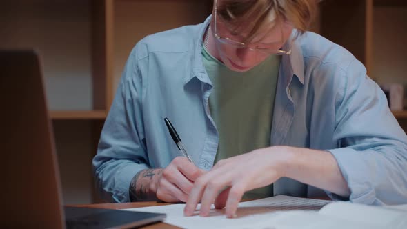 Young Man Searching Through the Textbook and Writing Notes Doing Homework