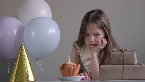 Sad Little Girl Celebrating Birthday Alone Over Background of Gifts and Balloons