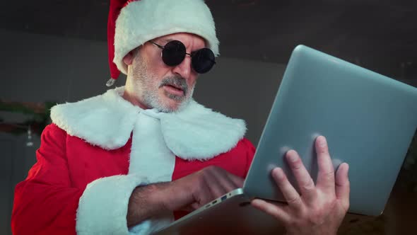 Cheerful Santa Clau in Black Glasses in Living Room and Chatting By Laptop with Video Chat.