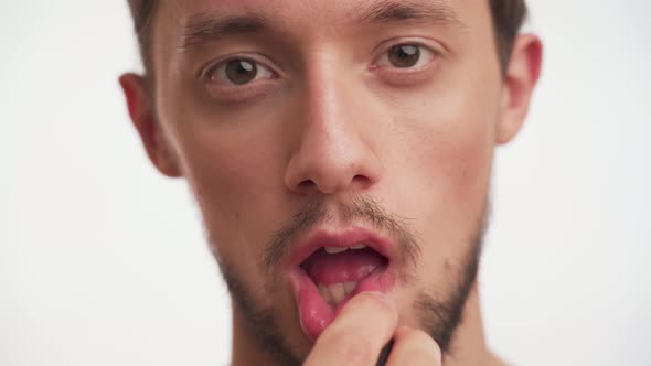 Bearded brunette man use lipstick, applying bright pink color isolated on white background close up