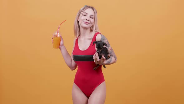 Sexy Blonde Girl in One Piece Red Swimsuit with a Cocktail in One Hand and a Dog in Another