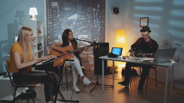 Multiracial Band of Friends Singing and Playing Musical Instruments in Cozy Home Studio 