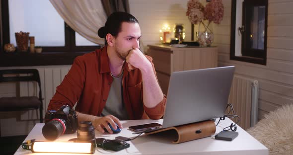 A Young Handsome Male Photographer and Videographer Works at Home on a Laptop