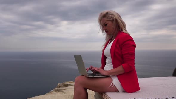 Well Looking Middle Aged Woman Typing on Laptop Keyboard Outdoors on Terrace with Beautiful Sea View