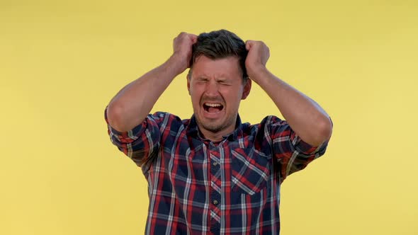 Young Man in Checkered Shirt Putting Fists on Head and Screaming in Pain