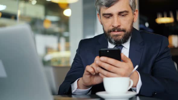 Bearded Office Worker in Suit Using Smartphone During Coffee Break in Cafe
