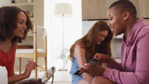 Diverse group of happy female friends trying makeup and talking at home