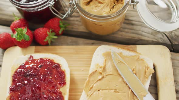 Peanut butter and jelly sandwich on wooden tray with milk and strawberries on wooden surface