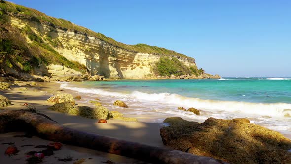 Breathtaking low flight above sandy rocky beach towards turquoise ocean waves and limestone sheer cl