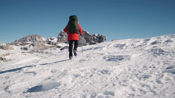 Hiker walks along snowy ridge high in the mountains filmed from behind