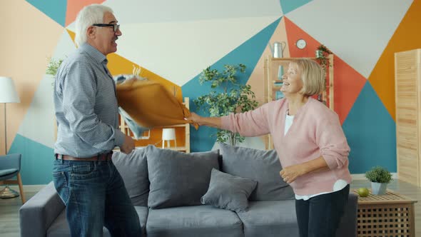 Playful Man and Woman Senior Couple Fighting Pillows Having Fun at Home