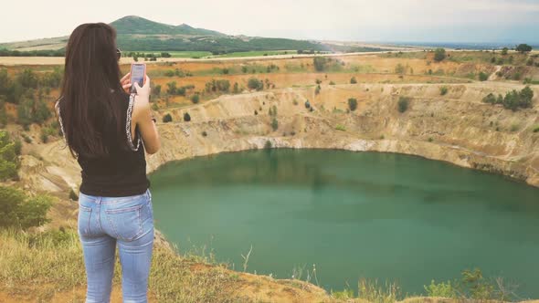 Back View of Young Woman Using Her Smartphone To Take Photos of Copper Open Mine Pit in Bulgaria