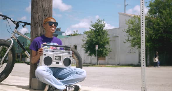 Panning shot of African American female holding boom box while sitting on ground