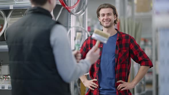 Portrait of Concentrated Handsome Client Choosing Paint Brush in Hardware Store Consulting Worker