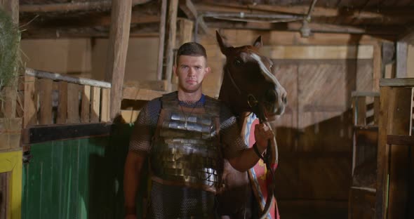 Portrait a Russian Soldier in Chain Mail Leads a Horse with a Shield and Spears