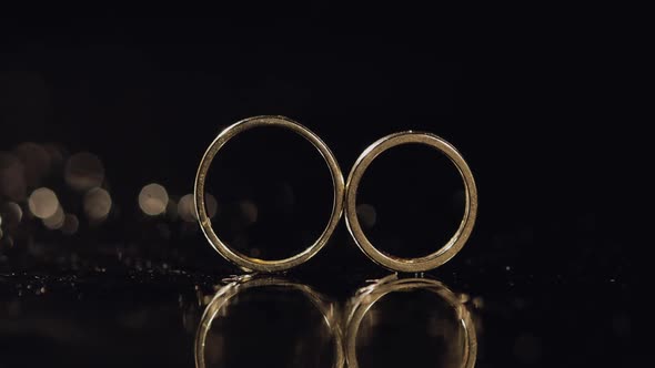 Wedding Rings on Dark Water Surface Shining with Light. Close Up Macro