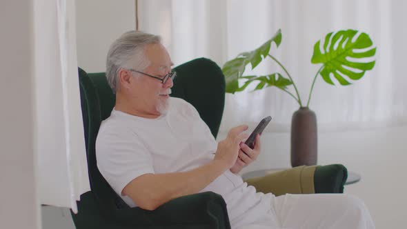 Happiness of wellness elderly asian man using mobile phone and social media smile at home