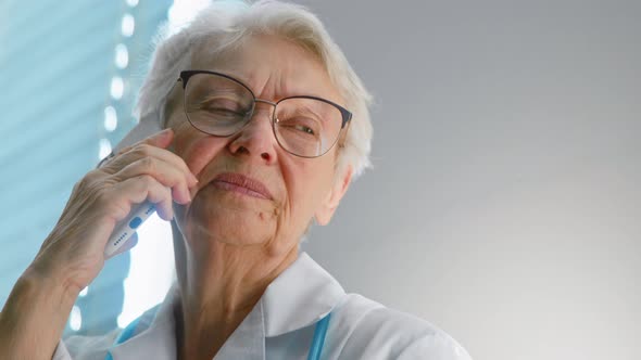 Cheerful senior doctor with eyeglasses talks on mobile phone