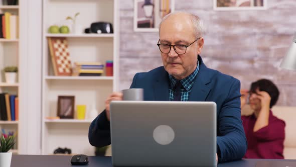 Old Man Enjoying a Cup of Coffee While Working on Laptop