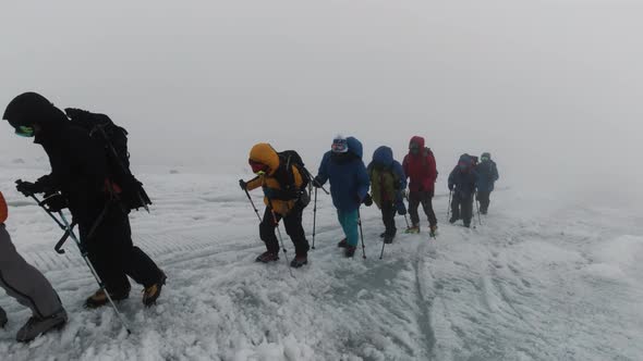 Group of extreme tourists walking one by one on icy surface of a hill