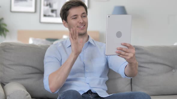 Online Video Chat on Tablet By Handsome Young Man Sitting on Couch