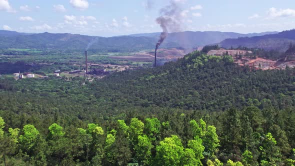 Aerial forward over verdant landscape with smoking chimneys in nickel mine, Loma Miranda. Falconbrid