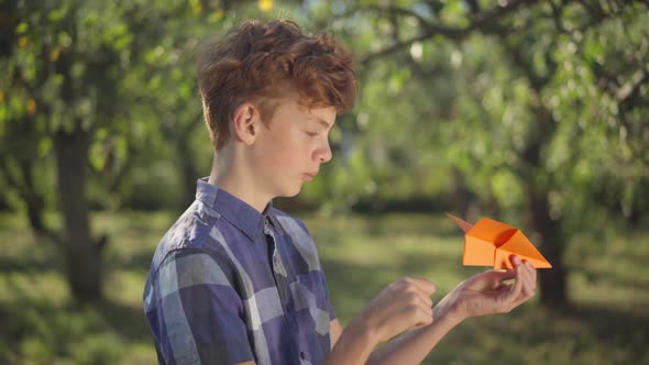 Side View Handsome Teenage Boy with Red Hair Launching Paper Plane Outdoors Looking Away